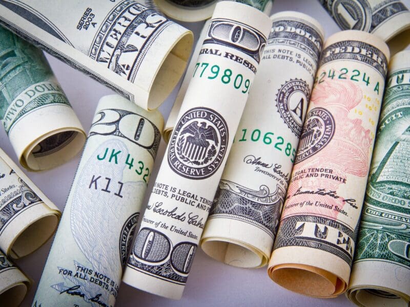 Rolled US dollar bills and a pen on a white surface. Rolled US dollar bills and a pen on a white surface.