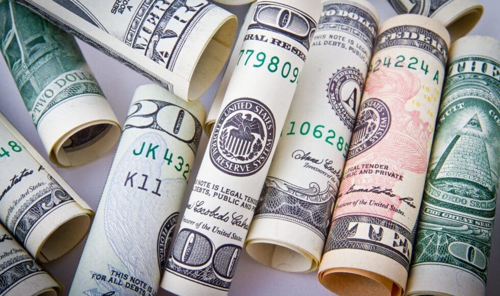 Rolled US dollar bills and a pen on a white surface.